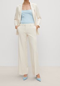 Crèmfärgad kavaj över en ljusblå linne, parat med crèmfärgade vida byxor. Ljusblå spetsiga klackar fulländar outfiten.