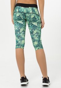Leggings capri verdes y negros con un patrón de hojas, con una cinturilla negra y un diseño ajustado, adecuados para ropa deportiva.