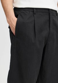 Pantalones negros hechos de tejido ligero con una textura suave, que cuentan con bolsillos laterales, un frente plano y un corte ajustado.