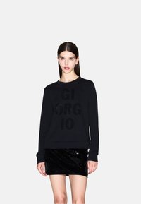 Sudadera negra con "GIORGIO" en lentejuelas texturizadas, con cuello redondo y puños acanalados, combinada con una minifalda negra de lentejuelas.