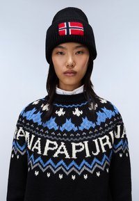Czarna dzianinowa czapka ozdobiona czerwoną flagą norweską; zdobiona czarna, niebieska i biała sweter dzianinowy z geometrycznymi wzorami i napisami.