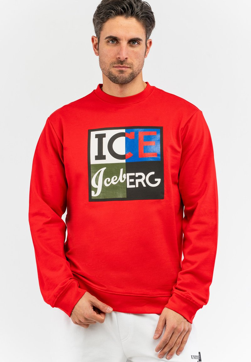 Rød sweatshirt med lange ærmer, der har et iøjnefaldende grafisk design med teksten "ICE" og "Iceberg" i forskellige farver, lavet af blødt bommateriale.