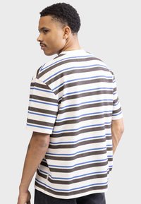 Striped t-shirt in cream, brown, and blue. Short sleeves, relaxed fit, textured fabric, and a small logo tag at the hem.