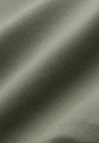 Tissu vert olive lisse avec un subtil nervurage diagonal et des plis doux qui créent des ombres délicates.