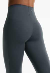Magas derekú, sötétszürke leggings sima, rugalmas anyagból, lapos varrásokkal és egy kis logóval a derékrészen.