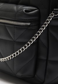 Czarna pikowana torebka na ramię z srebrnym łańcuszkowym paskiem i kieszenią na zamek. Wykonana z teksturowanego materiału o eleganckim designie.