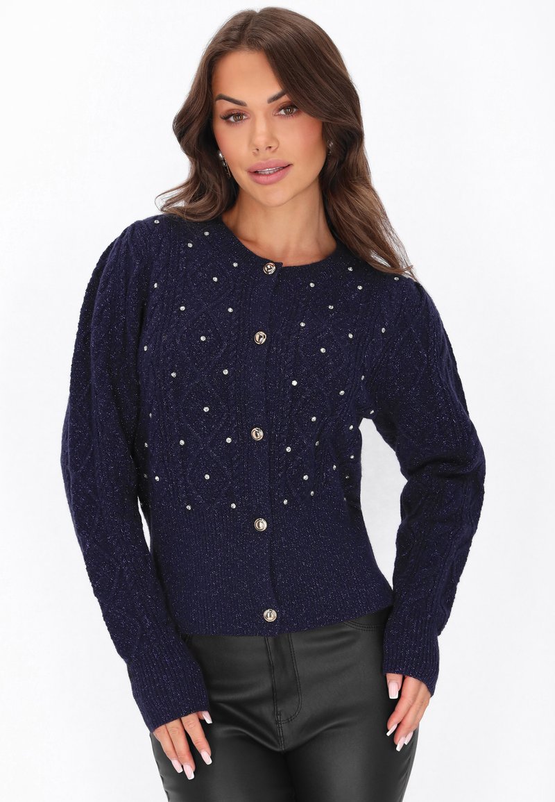 Merihenkinen neulejakku, jossa on teksturoitu kaapelikuvio, koristeltu pienillä helmillä, kultasävyiset napit ja ribbikuvioidut hihansuut.