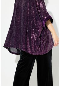 Top viola in paillettes con vestibilità ampia, maniche arrotolate e design testurizzato, abbinato a pantaloni in velluto neri.