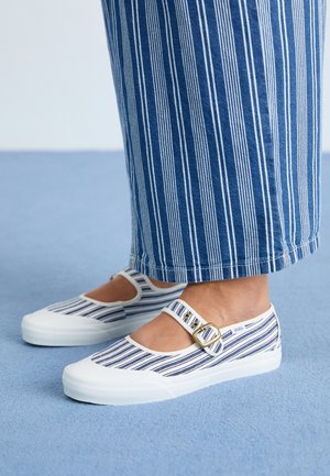 Zapatos Mary Jane a rayas azules y blancas con correas y hebillas, usados con pantalones a rayas de pierna ancha a juego sobre una alfombra azul.