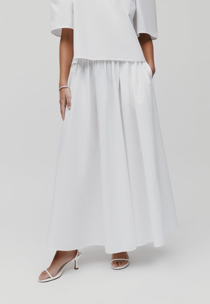 Witte, lange rok met een geraffineerde taille, gemaakt van een gladde stof. Gecombineerd met witte open teen hakken, met een slanke hak.