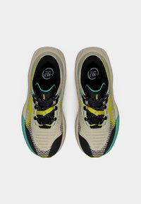 Ζευγάρι μπεζ αθλητικά παπούτσια με μαύρες, κίτρινες και τιρκουάζ λεπτομέρειες, μαύρα κορδόνια και λογότυπα της μάρκας στη γλώσσα και στην εσωτερική σόλα.