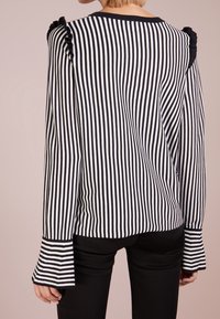 Top a maniche lunghe a righe bianche e nere con dettagli arricciati sulle spalle e polsini svasati, realizzato in un tessuto morbido e strutturato.