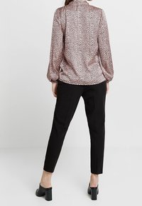 Blouse en imprimé léopard rose clair et marron, avec de longues manches bouffantes, rentrée dans un pantalon noir slim, complétée par des mules à talons épais.