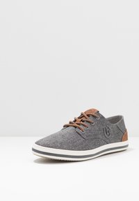 Chaussure décontractée en textile gris avec des accents en cuir marron et des lacets ronds. Dotée d'une semelle blanche avec une bande grise et un logo sur le côté.