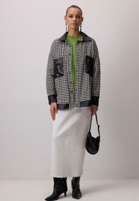 Jakna u crno-bijelom houndstooth uzorku s kožnim detaljima, zelena majica, bijela suknja i crne gležnjače. Uključuje malu crnu torbu.