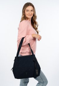 Borsa a mano in finta pelle blu navy con finitura testurizzata, manici neri, chiusura con zip e un accento decorativo a frange. Tasca con zip su un lato.