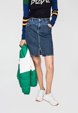 Denim-pitkähihainen hame, jonka etupuolella on halkio, paritettuna musta-sini-vihreään raidalliseen pitkähihahaiseen paitaan ja vihreään toppatakkiin. Valkoiset tennarit.