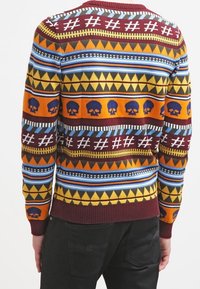 Maglione lavorato a maglia con motivi colorati di teschi e forme geometriche, principalmente in tonalità di arancione, marrone, blu e giallo, con polsini a coste.