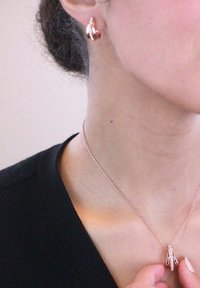 Halskette und passende Ohrringe aus Roségold, die ein zartes Design mit kleinen Akzenten aufweisen; glatte und glänzende Textur auf der Haut.