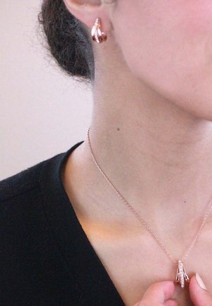 Collier en or rose et boucles d'oreilles assorties, arborant un design délicat avec de petites touches ; texture lisse et brillante sur la peau.