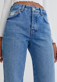 Jeans in denim di un blu chiaro a vita alta, caratterizzati da un classico design a cinque tasche con dettagli sfrangiati sulla tasca frontale e hardware color rame.