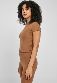 Brun ribbet top med korte flæseærmer og cropped kant, lavet af blødt stof, parret med matchende ribbet højtaljede bukser.