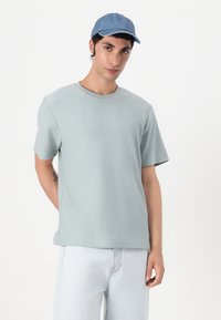 Light green short-sleeve T-shirt with a round neckline, made of soft material; paired with a denim blue cap, displayed against a neutral background.