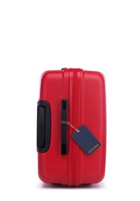 Maleta rígida roja con superficie texturizada, cierre de cremallera, asa lateral y una etiqueta de marca azul adjunta. Forma compacta y rectangular.