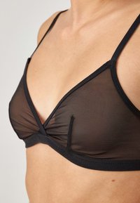 Zwarte doorzichtige bralette met driehoekige cups, dunne verstelbare bandjes en gerimpelde details in het midden. Zachte stoftextuur en elastische band.