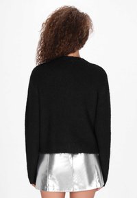 Czarny dziany sweter o luźnym kroju, z opadłymi ramionami i prążkowanym wykończeniem. Połączony z błyszcząca srebrną mini spódnicą.