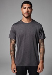 Camiseta deportiva gris oscuro con textura suave, mangas cortas, cuello redondo y un sutil patrón horizontal. Presenta un pecho y brazos visibles.