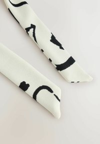 Extrémités d'une écharpe en tissu blanc avec des lignes et formes abstraites noires irrégulières sur un fond clair uni.