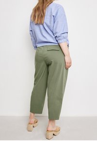 Olivově zelené zkrácené kalhoty volného střihu s kapsou na zadní straně, doplněné světle modrou a bílou pruhovanou oversized košilí. Hnědé sandály na platformě.