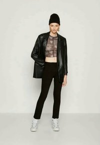 Svart skinn oversized blazer over en kort grå og brun mønstret topp, svart slim-fit bukser og hvite sneakers. Modell som har på seg en beanie.