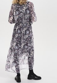 Lång, genomskinlig klänning med ett paisleymönster i lila, svart och grått, med en samlad midja och puffärmar. Bärs med svarta skor.