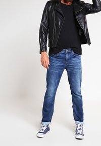 Chaqueta de motorista de cuero negra sobre una camiseta negra, combinada con jeans azules y zapatillas navy. Los jeans están ligeramente doblados en los puños.