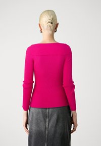 Pull ajusté en maille côtelée de couleur rose vif avec des manches longues et un décolleté carré, associé à une jupe en denim foncé. Texture lisse, détails minimalistes.