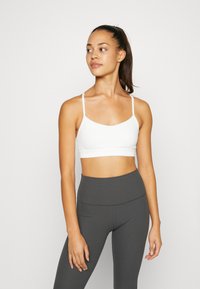 Balts sporta krūšturis ar regulējamām plāniem siksniņām un gludu tekstūru, kombinēts ar augsto vidukli, ribotu, tumši pelēku biksēm.