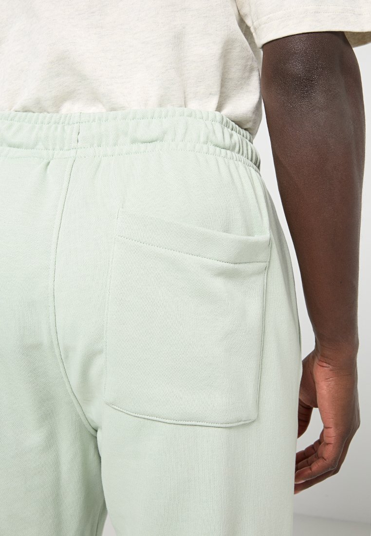 Pantaloni della tuta verde chiaro con cintura elastica, dotati di una singola tasca sul retro e un tessuto liscio e strutturato.
