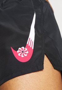 Shorts de sport noirs avec un logo blanc et rose agrémenté de détails floraux. Fabriqués en tissu lisse avec un léger brillant et des fentes sur les côtés.