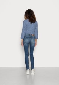 Suéter corto azul con tejido de punto texturizado, combinado con jeans ajustados de color azul oscuro con dobladillo deshilachado y parche de cuero marrón. Zapatillas blancas gruesas.