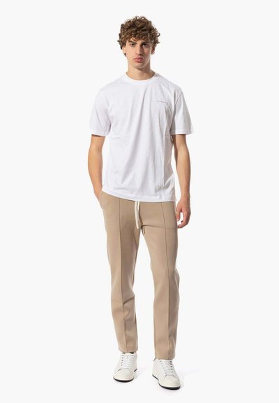 T-shirt bianco in cotone con una stampa sottile, abbinato a pantaloni felpati beige con un design affusolato e vita elastica, indossati con sneakers bianche.