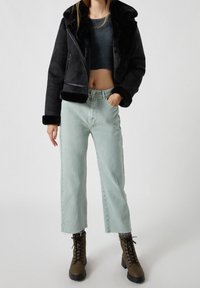 Černá kabát s umělou kožešinou podšitou, se zkráceným střihem, spárovaný se světle zelenými džíny s vysokým pasem a hnědými šněrovacími botami s masivními podrážkami.