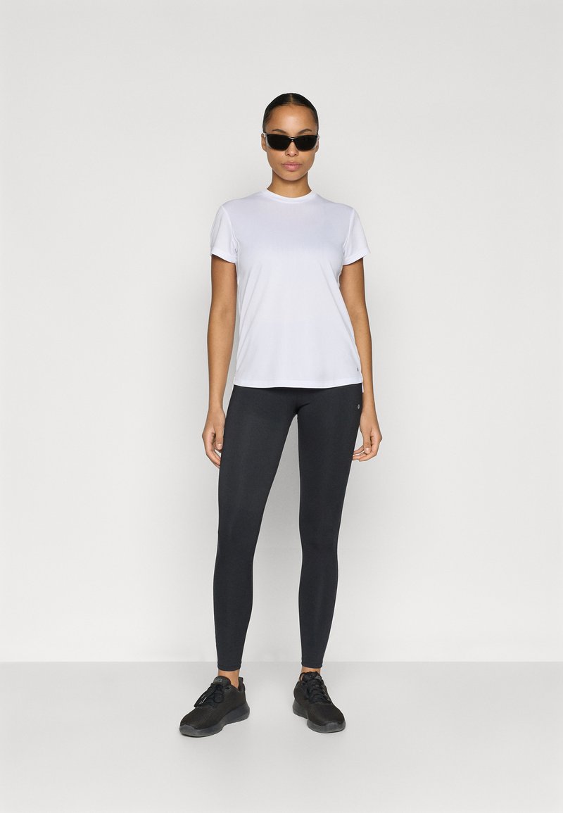 Weißes T-Shirt mit kurzen Ärmeln, schwarze Leggings und schwarze Sneakers. Glatter Stoff, figurbetontes Design und minimale Akzente mit moderner Silhouette.