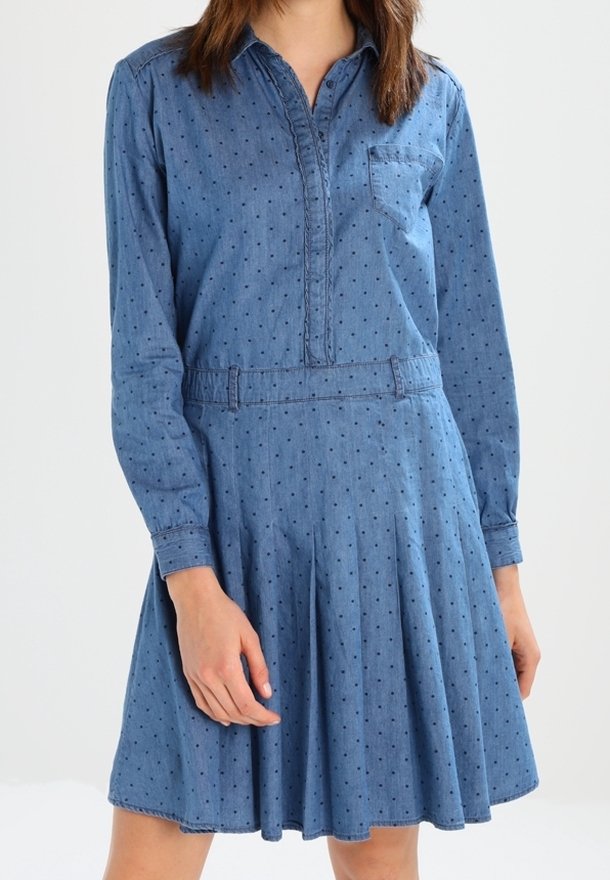 Jeansklänning med långa ärmar, spetsig krage och framficka. Har små prickar och en utsvängd kjol, vilket ger en avslappnad passform.