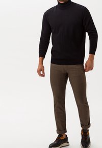 Black turtleneck sweater paired with light brown trousers, showcasing a smooth texture. Accented with black and orange sneakers.