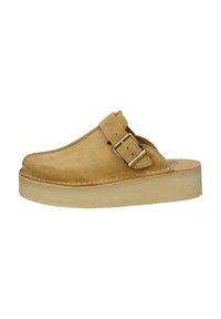 Scarpa slip-on in suede beige con punta arrotondata, cinturino regolabile con fibbia e suola piatta di colore chiaro, caratterizzata da cuciture lungo il bordo.