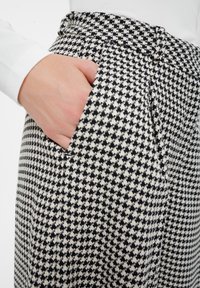 Czarno-białe spodnie w wzór houndstooth z wysokim stanem, z bocznymi kieszeniami i gładką fakturą.