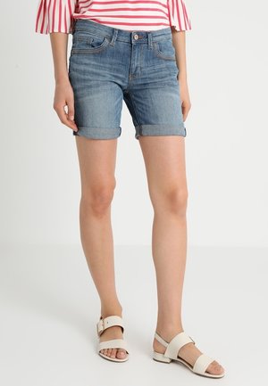 Lichte blauwe denim shorts met opgerolde omslagen en voorkezen. Draagt een top met roze en witte strepen en beige sandalen.