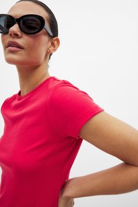 Raudonas raštuotas trumpomis rankovėmis viršus su apvaliu iškirpimu, derinamas su juodais per dideliais akinių nuo saulės rėmeliais. Lygus paviršius; prigludęs siluetas.